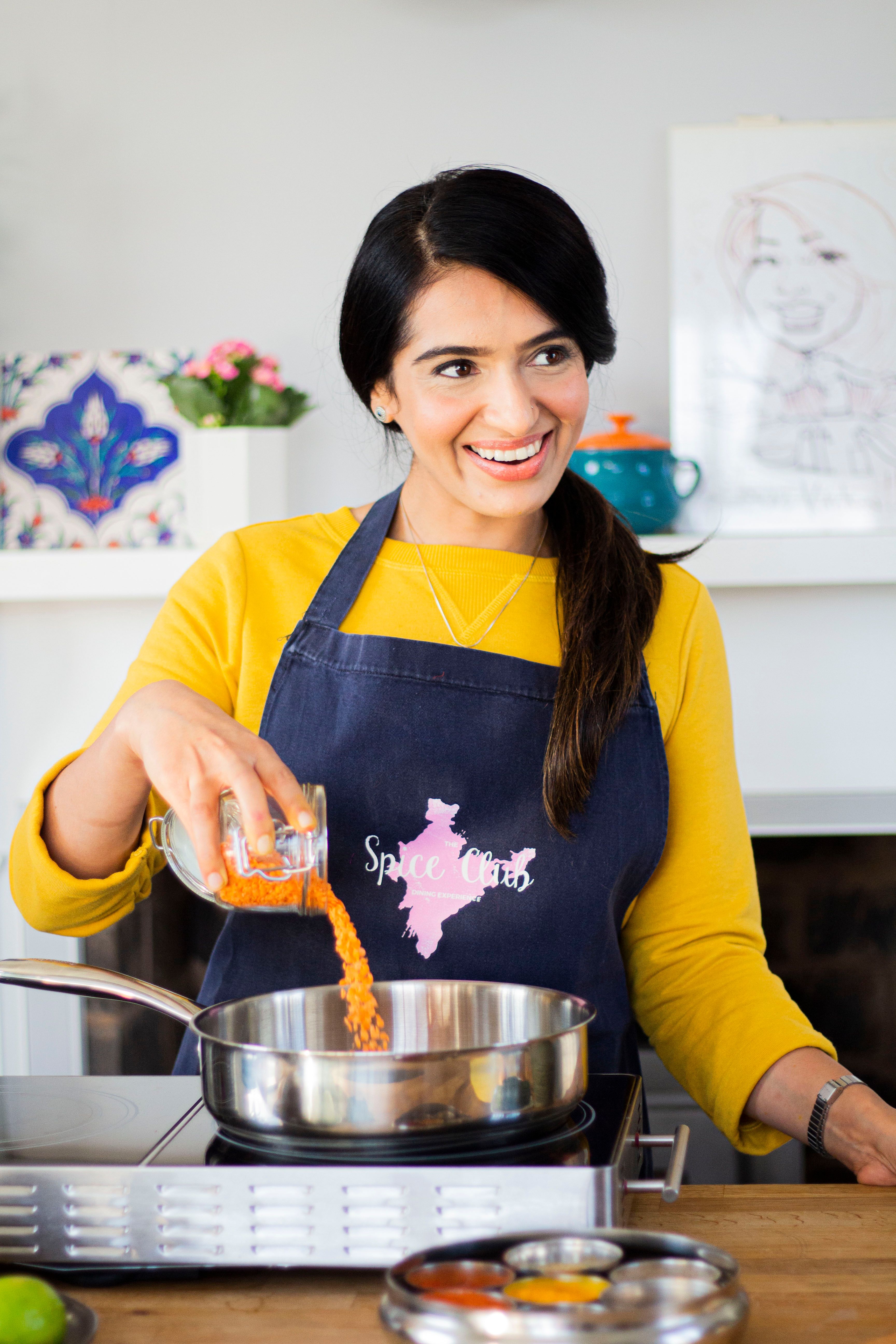 Monica teaching at The Spice Club cookery school, pouring spices into a pan